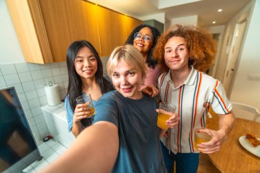 Dört farklı arkadaş modern bir mutfakta meyve suyu içerken selfie çekiyorlar.