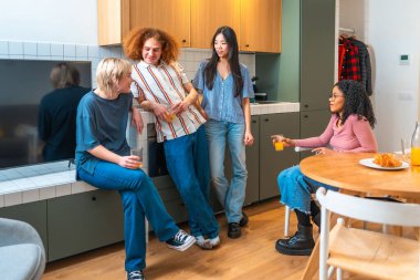 Dört oda arkadaşı modern mutfaklarında gündelik bir sohbetin tadını çıkarıyorlar meyve suyu içip kahvaltı ediyorlar.