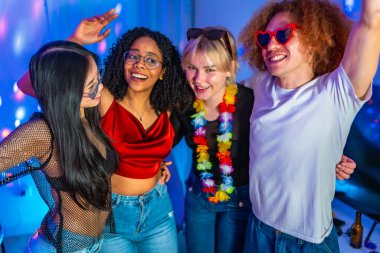 Dört neşeli çoklu etnik arkadaş dans ediyor ve mavi disko ışıkları olan bir partide eğleniyorlar.