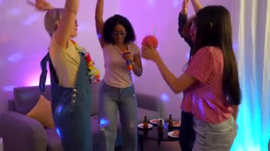 Kadın arkadaşlar enerjik bir karaoke atmosferi yaratıyor, ev partisi ortamında şarkı söyleyip dans ediyorlar, neşeli anları müzik, içki ve bulaşıcı coşkuyla paylaşıyorlar.