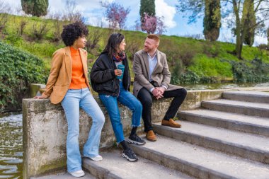 İş çıkışı kanalda sohbet edip kahve içen üç genç profesyonel iş hayatı dengesi ve şehir yaşam tarzını temsil ediyor.