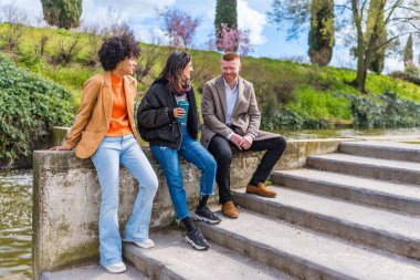 Üç genç profesyonel, bir şehir parkında sohbet ediyor ve birlikte gülüyorlar.