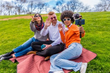 Parkta akıllı telefon ve harici mikrofon ile video sallayan ve çeken üç içerik oluşturucu