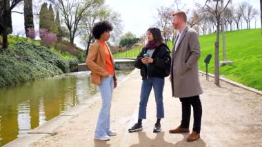 Huzurlu şehir parkı göletinin yanında sıcak sohbetler eden arkadaşlar, hafta sonu bağlantının sakin olduğu yerde sürdürülebilir kahve fincanları tutuyorlar.