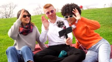 Milenyumlar, arkadaşlarıyla birlikte podcast kaydında, güneşli park ortamında dijital içerik ve paylaşımlı tutku yaratmada işbirliği yapıyorlar.