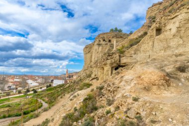 Kumtaşı mağaraları bir yamaçta oyulmuş Navarre, İspanya 'da bulutlu mavi bir gökyüzünün altında tartışmaların resim gibi köyüne bakıyorlar.