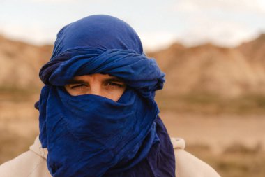Sahara Çölü 'nün engin ve kurak manzarasına karşı çivit bir tagel taşıyla süslenmiş bir Tuareg erkeğinin portresi.