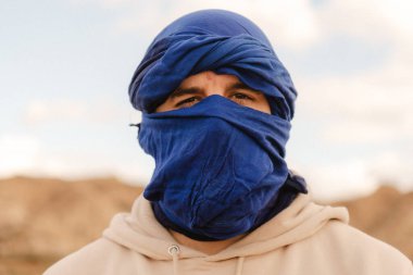 Mavi sarıklı, bej kapüşonlu turist çöl manzarasına bakıyor.