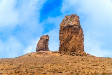 Dağ yolunda yürüyen turistler Roque Nublo 'ya, Büyük Kanarya' da bir volkanik kaya oluşumuna, kanarya adalarına, İspanya 'ya, mavi gökyüzünün altında bulutlarla birlikte yürüyorlar.