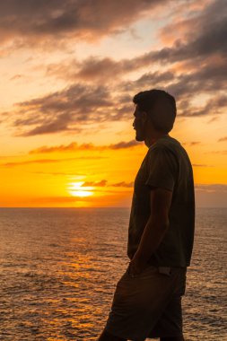 Bir turistin silueti Atlantik okyanusu üzerinde güzel bir günbatımının keyfini çıkarıyor. Sahil kasabası Ağa, Büyük Kanarya, Kanarya Adaları, İspanya