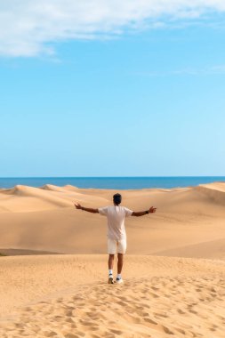 Genç adam maspaloma kumullarında kollarını açıyor, Büyük Kanarya, özgürlüğü hissediyor ve çöl manzarasının tadını çıkarıyor.