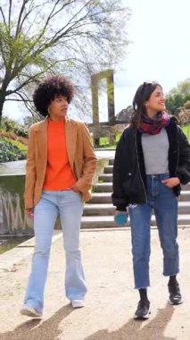 Parkta birlikte yürüyen genç kadın ve işadamı güneşli ve boş zamanların tadını çıkarırken arkadaşça sohbet ediyorlar.