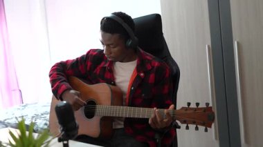 Genç müzisyen akustik gitar ve mikrofonla ev stüdyosunda müzik besteleyip kaydediyor.
