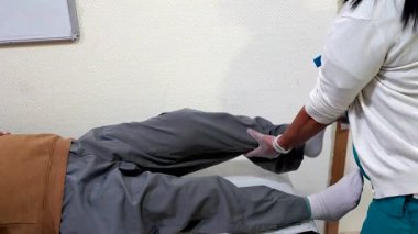 Profesyonel hemşire, bacak egzersizleri sırasında yaşlı adama destek olur, huzur evinde dolaşmayı ve iyileşmeyi teşvik eder.