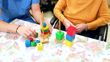 Hemşire yaşlı bir kadına renkli yapı taşlarıyla oynaması, bilişsel becerileri geliştirmesi ve huzurevine yerleştirilmesi için yardım ediyor.