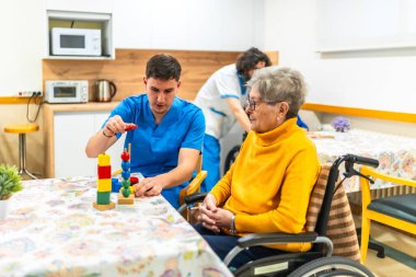 Hemşire, huzurevinde renkli ahşap oyuncaklar kullanarak idrak egzersizleri yapan yaşlı bir kadına yardım ediyor.