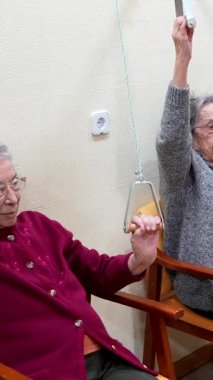 Üst düzey hastalar, bakım evlerindeki rehabilitasyon programlarının bir parçası olarak hemşirelerin de yardımıyla makara ile kol egzersizleri yapıyorlar.