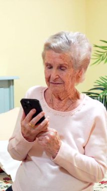 Huzurevi yatak odasında dinlenirken akıllı telefondan iletişim kuran, dijital dünyayla iletişim kuran ve emeklilik süresince sosyal olarak aktif olan üst düzey bir kadın.