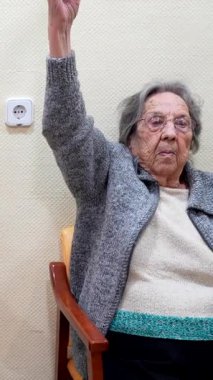 Son sınıf öğrencisi kadın, koluyla makara kullanarak egzersiz yapıyor, huzurevinde bir sandalyede oturuyor.