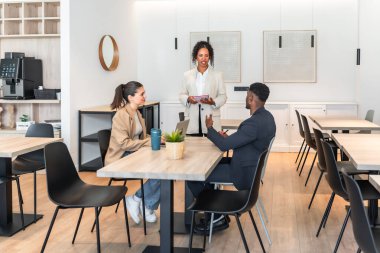 Üç meslektaş modern bir ofis alanında bir proje üzerinde çalışıyorlar ve başarı için strateji oluşturuyorlar.