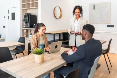 Çok ırklı iş adamları bir proje üzerinde birlikte çalışıyorlar, dizüstü bilgisayar kullanıyorlar ve modern bir ofiste not alıyorlar.