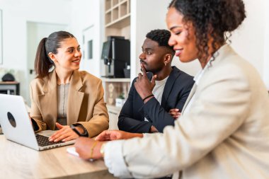 İş ekibi dizüstü bilgisayarla proje üzerinde çalışıyor, fikirleri ve stratejileri modern ofiste tartışıyor.