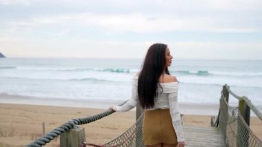 Tahta iskelede yürüyen şık bir manken, yaz tatilinde okyanus manzarasını tasasız bir zarafetle kucaklıyor.