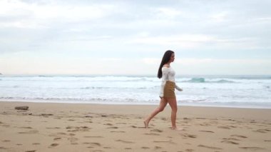 Çıplak ayaklı manken kumlu sahil şeridinde geziniyor, okyanus dalgaları yakınlarındaki kaygısız yaz yaşam tarzını şekillendiriyor manzaralı arka planda.