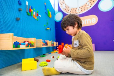 Anaokulu öğrencisi renkli inşaat oyuncaklarıyla canlandırıcı bir oyun alanında inşa etmeye konsantre oluyor.