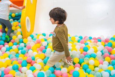 Neşeli bir top havuzunda oynayan genç bir çocuk, hayal gücü ve mutluluğu ateşleyen renkli bir oyun alanıyla çevrili.