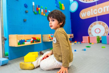 Anaokulu öğrencisi yerde oturmuş renkli inşaat oyuncaklarını keşfediyor, hayal gücünü arttırıyor ve canlandırıcı bir oyun alanında erken çocukluk gelişimi sağlıyor.