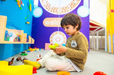 Anaokulu öğrencisi renkli plastik bloklar üzerine yoğunlaşarak canlandırıcı bir oyun alanında iyi motor beceriler geliştiriyor.