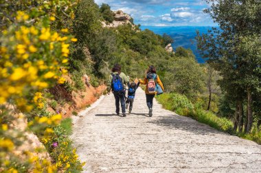 Sırt çantalı bir aile Montserrat 'ta bir dağ yolunda yürüyor, manzaranın ve temiz havanın tadını çıkarıyor.