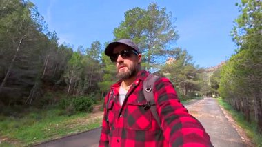 La Fontcalda 'da, Gandesa, Tarragona' da bir tapınak olan ormanın yakınındaki yolda yürüyen bir turist.