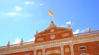 Rüzgarda dalgalanan katalan bayrağı güneşli bir günde açık mavi gökyüzünün altında tarihi tarragona belediye binasının ön cephesine doğru dalgalanıyor.