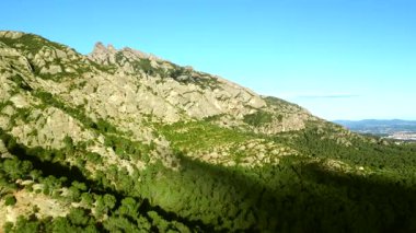Montserrat Massif 'in etkileyici görüntüsü, eşsiz kaya oluşumlarını ve berrak mavi gökyüzünün altındaki canlı yeşil ormanını gözler önüne seriyor.