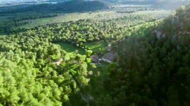 Gün ışığı giderek Montserrat kitlesini aşıyor, sakin dağ arazisi ve uzak bitki örtüsüyle yeşil kırsal alanda aşamalı gölgeleri ortaya çıkarıyor.