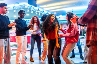 Neşeli çoklu etnik arkadaşlar neşeli bir şekilde dans ediyor ve eğlenceli bowling salonunda eğleniyorlar. Unutulmaz anılar yaratıyorlar.