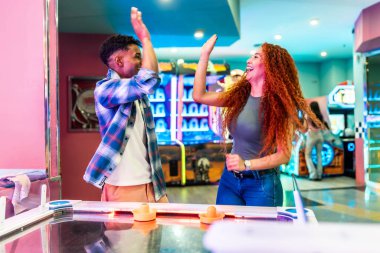 Canlı bir eğlence merkezinde hava hokeyi oynarken iki arkadaş beşlik çakıyor. Bir puanı ya da zaferi kutluyorlar.