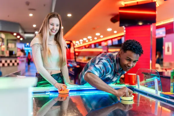 Renkli bir eğlence merkezinde hava hokeyi oynayarak eğlenen çeşitli arkadaşlar.