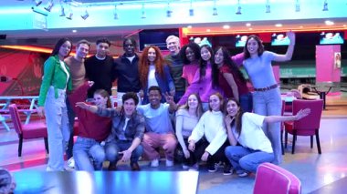 Genç çok kültürlü arkadaşlar birlikte poz veriyor, haftasonu sosyal toplantıları sırasında modern bowling salonunda neşeli anları paylaşıyor, hareketli enerjili grup fotoğraflarını çekiyorlar.