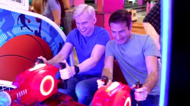 Genç erkek arkadaşlar rekabetçi bir yarış oyunu oynuyorlar, simülatör oyun makinesinde heyecan içinde geziniyorlar ve birbirlerine meydan okurken neşeyi paylaşıyorlar.