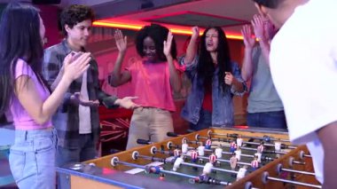 Çeşitli arkadaş grupları zaferi kutlarken langırt oynuyorlar, coşkulu etkileşimlerle coşkulu oyun salonunda heyecan ve neşeyi paylaşıyorlar.