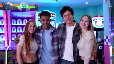 Çok ırklı bir grup arkadaş, eğlenceli atari salonlarında neşeli anlar paylaşıyor, renkli neon ışıkları ve bayram Cadılar Bayramı atmosferinde kaynaşıyorlar.