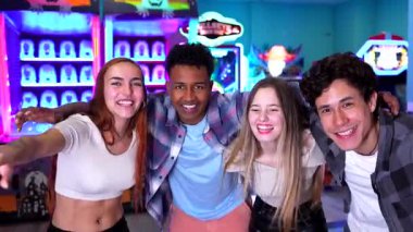 Genç arkadaşlar canlı oyun salonunun içinde neşeli anlar paylaşıyorlar, renkli neon ışıklı arka planla eğlenceli vakit geçirirken poz veriyorlar ve gülümsüyorlar.