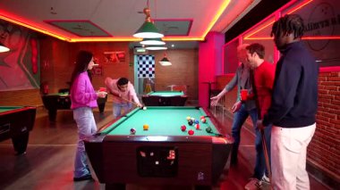 Çeşitli arkadaşlar bilardo oynuyorlar, neşeli bilardo salonunda kahkaha ve rekabetçi ruh paylaşıyorlar, sosyal bağlantı ve neşe sergiliyorlar.