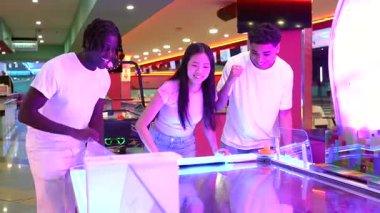 Havalı bir hava hokeyi maçına katılan genç arkadaşlar, canlı neon ışıklı oyun alanı kullanarak canlı atari salonunda rekabetçi enerji ve yoldaşlık sergiliyorlar.