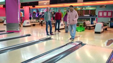 Bowling meraklısı mükemmel bir vuruş yapıyor, enerjik eğlence anında destekleyici arkadaşlardan yüksek sesle tezahürat yapıyor.