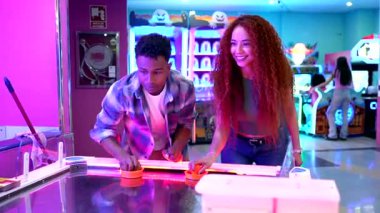 Genç çift hava hokeyi oynuyor, neşeli atari oyunlarından zevk alıyor ve coşkulu eğlence merkezinde hünerlerini sergiliyor.