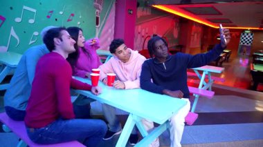 Genç arkadaşlar unutulmaz anları yakalıyor, neon ışıkları ve neşeli atmosferle çevrili bowling pistlerinin yakınında selfie çekerken kahkaha ve heyecan paylaşıyorlar.